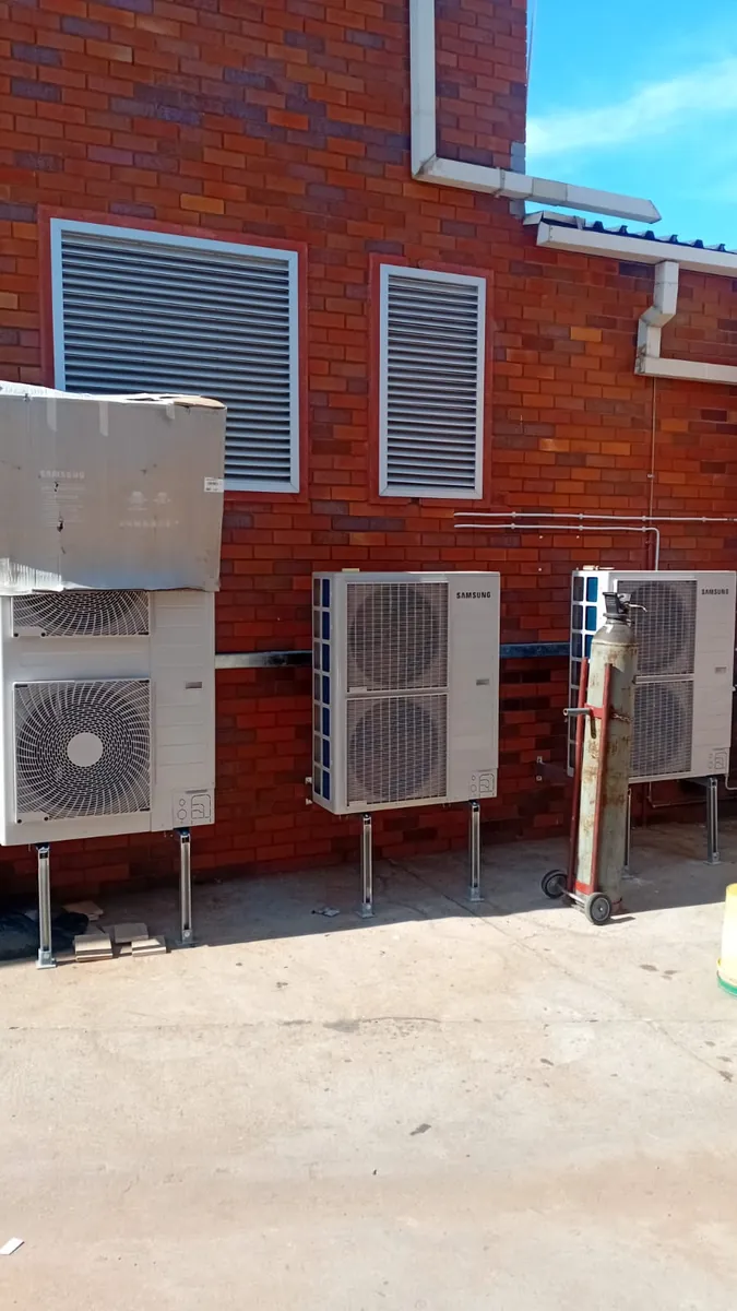 Three outdoor air-conditioning units mounted on the brick wall of a commercial building